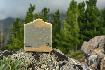 Piece of craft soap on the background of mountains, forests and sky. Concept of the image of organic cosmetics in a natural environment