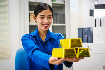 An Asian businesswoman is sitting at her desk in the office,analyzing gold bullion prices,market trends,investment factors,providing in-depth analysis adjust trading strategies for positive returns.