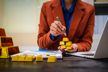 An Asian businesswoman is sitting at her desk in the office,analyzing gold bullion prices,market trends,investment factors,providing in-depth analysis adjust trading strategies for positive returns.