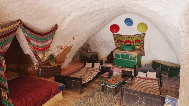 Modestly furnished cozy sleeping area in ancient Berber cave dwelling in Matmata, with double bed for home owners, decorated with traditional textiles. History of indigenous peoples of Tunisia. High