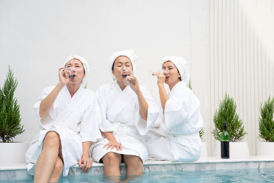 Middle-aged Asian women friends enjoy a pool party, holding glasses of wine and dancing. This vibrant scene radiates with friendship, relaxation, and the joy of sharing special moments together.