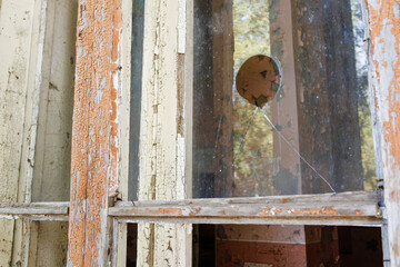 Broken glass in the window of an old house. Close-up. Old wooden window frame with peeling paint and broken glass. An abandoned interior can be seen through the broken windows.