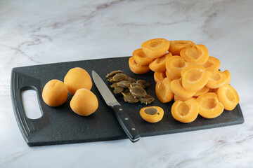 Preparation of apricots for jam or filling for baking. Pile of halves apricots, extracted kernels, a fruit knife on a cutting board, close-up, high resolution.
