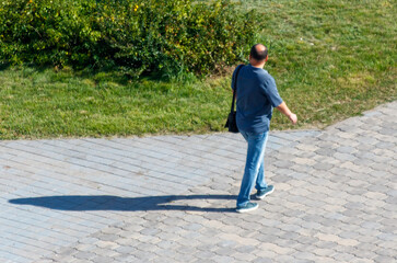 Naklejka premium A man wearing a blue shirt and jeans walks on a brick walkway