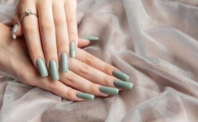 Fototapeta premium Elegant hands with long green nails resting on soft fabric