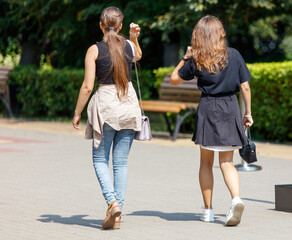 Two women walking down a sidewalk, one of them carrying a purse