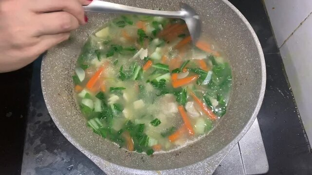 Cooker is making a healthy soup dish from juicy vegetables , Close-up of mixing various colorful vegetables in a pan.