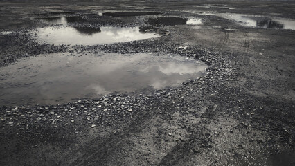Wheel tracks on dirt road surface. Mud puddle on the damaged way. The road condition is pothole.