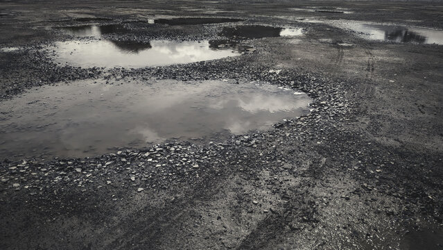 Wheel tracks on dirt road surface. Mud puddle on the damaged way. The road condition is pothole.