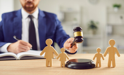 In family court, a lawyer delivers a verdict on divorce proceedings, wielding a gavel, beside wooden family figurines, symbolizing legal judgement regarding custody, children, and justice.