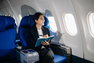 Asian businesswoman or entrepreneur in a formal suit on an airplane sitting in business class using a phone, computer laptop. Travel in style, work