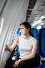 Attractive Asian female passenger of airplane sitting in comfortable seat while working laptop and tablet. Travel in style, work with grace.