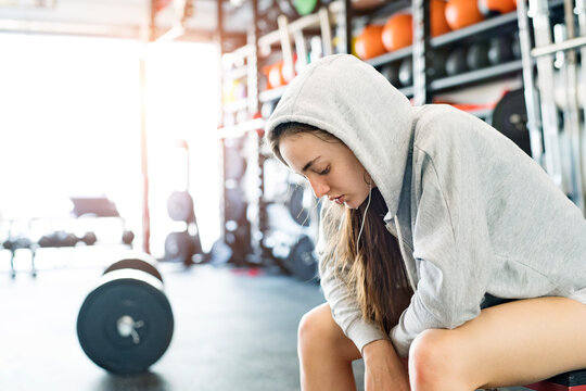 Young fitness girl with sweat on face feeling exhausted after hard workout in gym, sitting and listening music, breathing exercise.