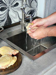 Close-up a man washes chicken meat in a sink in his home kitchen.