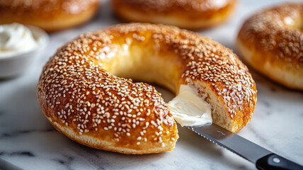 A sesame bagel with cream cheese being spread with a knife.