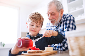 Boy and grandpa making breakfast in the kitchen. Grandfather spending time with grandson, taking care of him while parents are at work.