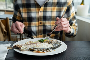 close up of man eating cooked fish in restaurant