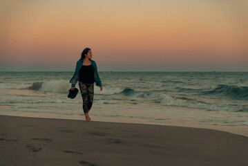 Woman walks barefoot along the seashore to feel the water on her feet.