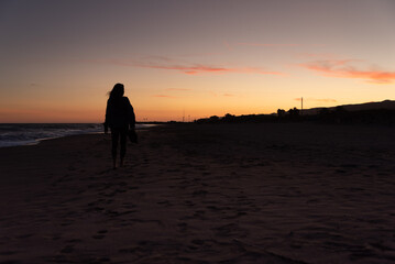 Silhouette of a woman walking on the beach with a golden sky.