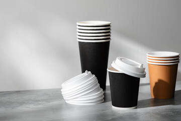 Stack of coffee cups in various colors with lids on a gray surface