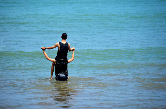 two men in black are carrying out activities on the beach