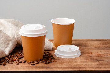 Disposable coffee cups placed on a wooden board with scattered coffee beans and a newspaper