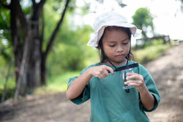 A young girl is holding a magnifying glass and looking at something in a glass