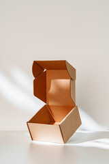 An open cardboard box rests on a bright white surface with soft shadows highlighting its edges and structure in natural light