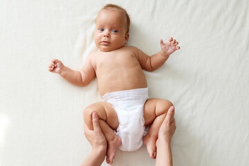 Unrecognizable caring mother making gymnastics to her newborn baby on white sheet at home unknown woman helping infant kid to relieve gas doing exercises with little kid to prevent child constipation