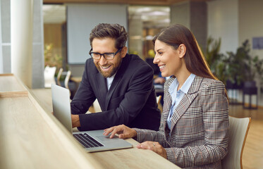 Company employees working at same desk in a modern office looking at laptop monitor screen discussing work projects. Young business people coworkers working on their workplace having a meeting.