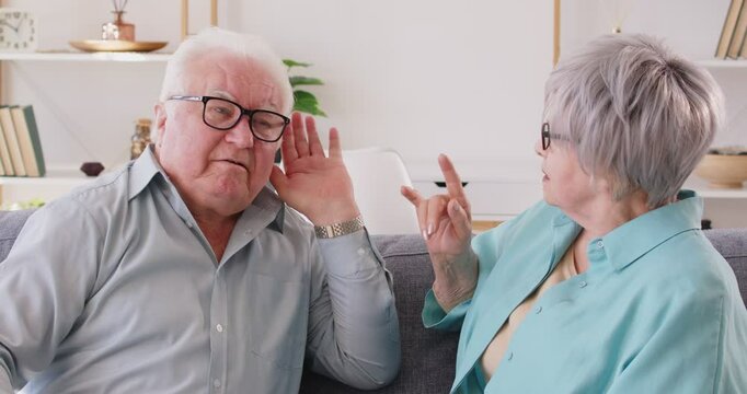 Hearing loss problem, senior couple talking, aging symptoms and causes, communication disabling. Aged old retired pair talking, speaking at home, unable to understand wife speech, ear problem