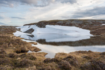 A small pond in the mountains on a calm and windless early summer day with lingering snow on the slope, Vardø, Varanger Peninsula National Park
