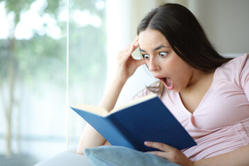 Amazed woman reading a aper book at home