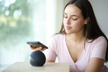 Fototapeta premium Serious woman pairing smart speaker with phone