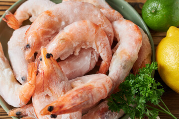 Frozen shrimp and parsley on a wooden table, close-up.