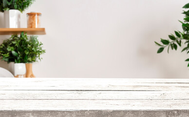 White wooden table with a blurred background of a shelf with plants and a white wall.
