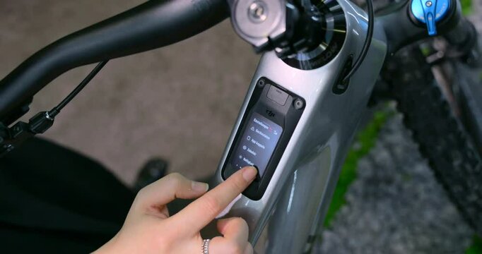 Close-up of a person using the control display on an electric bike to navigate through settings and menu options.