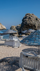 Sunlight shines on beach umbrellas and lounge chairs set on the sandy shore near rocky cliffs, inviting relaxation and enjoyment