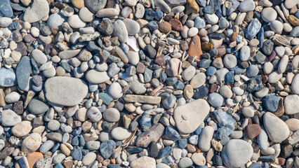 An array of smooth stones in various shapes and colors covers the sandy surface, reflecting sunlight during the day
