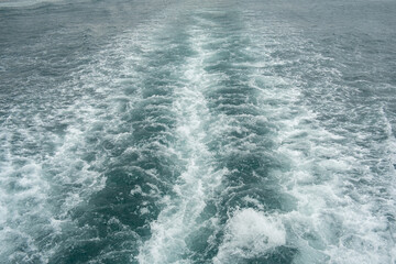 Rippling waves create dynamic patterns behind a boat as it moves through a serene sea under an overcast sky