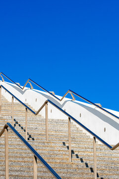 A steep staircase with white and beige color palette tilts towards an intensely blue sky, representing a blend of everyday architecture and clear, open spaces.