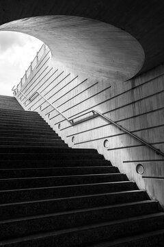 Fototapeta A captivating black and white photograph features an upward leading staircase within a curved architectural structure, evoking a sense of mystery and elegance.