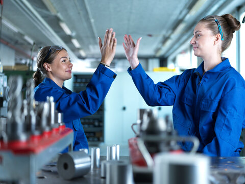 Smiling metal workers giving high-five at factory