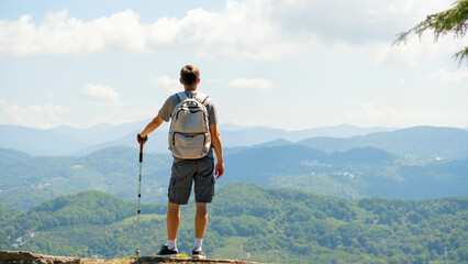 Naklejka premium A man stands on observation deck with walking sticks and contemplating the mountains.