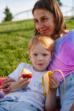 Cute boy eating fruits and sitting with mother at park