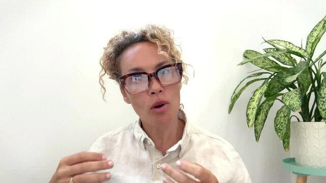 Female teacher with tied hair and glasses scolds irritated student during daylight, 48-year-old woman sitting and speaking, classroom scene, strict educator, disciplinary action, unhappy student 