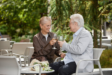 Happy couple toasting with wine glass and sitting near table at outdoor restaurant