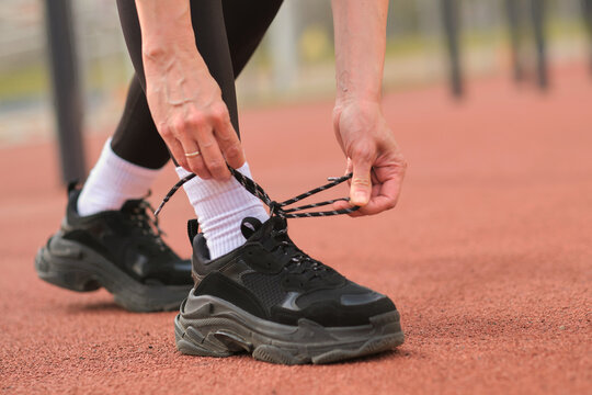 A close-up shot of a woman tying her shoelaces before starting a workout on an outdoor track. This image reflects the preparation and focus required for an active and healthy lifestyle.