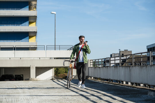 Smiling man talking on smart phone and walking with bicycle