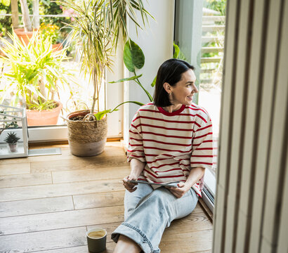 Smiling woman looking out of window sitting at home